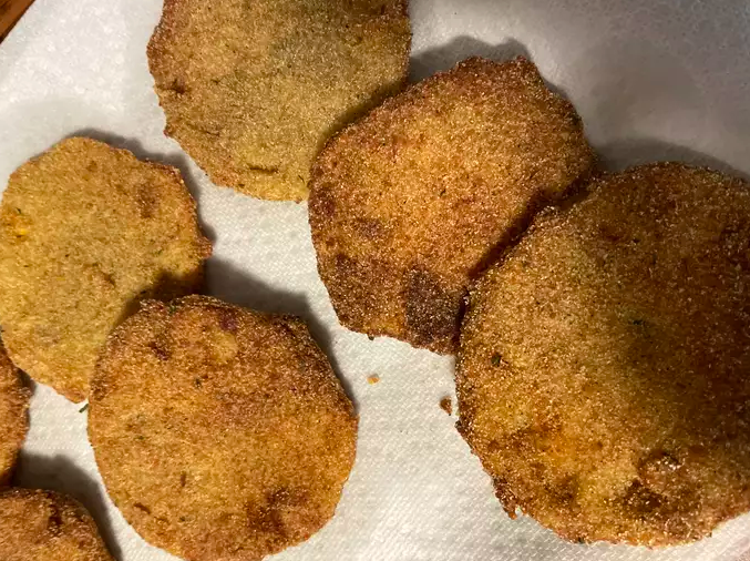 A plate of fried green tomatoes sitting on top of a paper towel. The tomatoes are coated in a golden brown breading and fried to perfection. They are served with a side of dipping sauce.